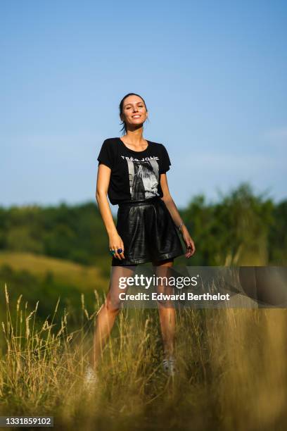 Landiana Cerciu wears a black and white t-shirt with a printed picture and the slogan "Tres Jolie", black leather mini shorts, on July 26, 2021 in...