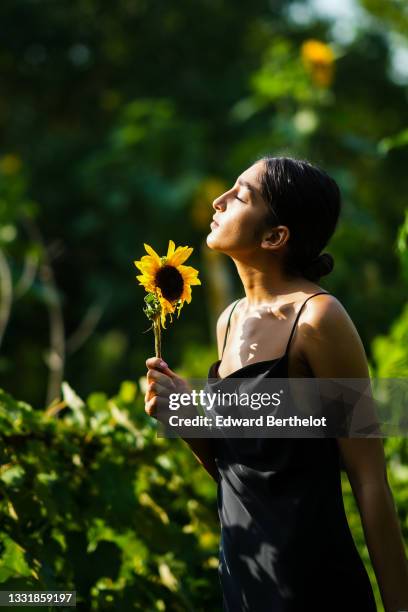 Jacqueline Barth wears a black lustrous silky long dress, holds a sunflower, on July 26, 2021 in Sibiu, Romania.