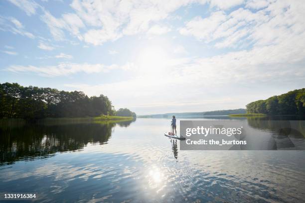 woman stand up paddling on an idyllic lake in summer, clouds and blue sky are reflected in the smooth water - sup stock pictures, royalty-free photos & images