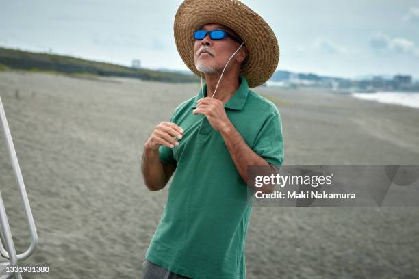 a portrait of a senior man wearing a straw hat on the beach. - beach top view stock-fotos und bilder
