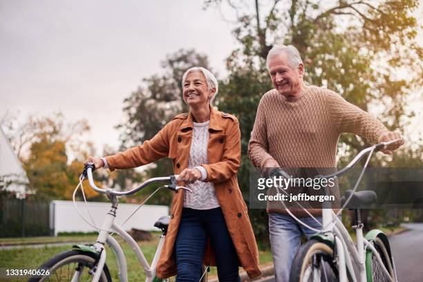 shot of a mature couple taking a bike ride at sunset - adult riding bike through park stock pictures, royalty-free photos & images