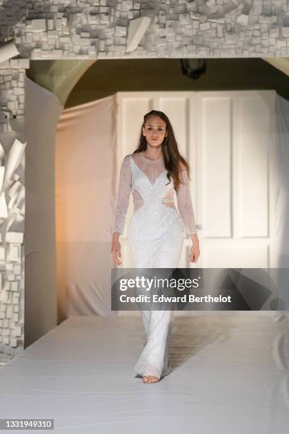 Model walks the runway and wears a tulle with white embroidered sequins V-neck / cut-out / long sleeves / long dress, brown shiny ruffled leather...