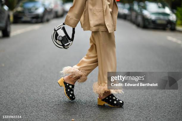 Gabriella Berdugo wears a beige Pyjama suit with feathers details at hems from Sleepers, black clogs / sandals with floral print, a black and white...