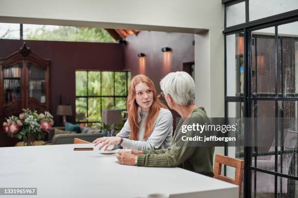 shot of a young woman having coffee with her elderly mother at home - mature woman daughter stockfoto's en -beelden