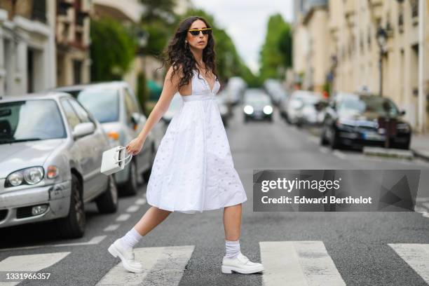 Gabriella Berdugo wears a white strappy sleeveless white low-neck midi pleated / gathered dress from Prada with round keyholes, white socks, white...