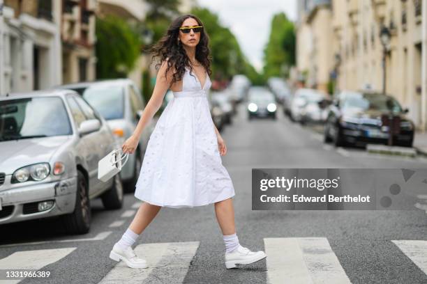 Gabriella Berdugo wears a white strappy sleeveless white low-neck midi pleated / gathered dress from Prada with round keyholes, white socks, white...