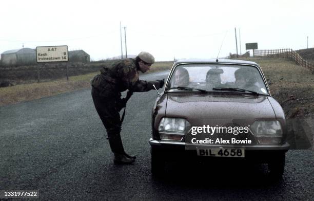 In the pouring rain a British soldier checks the driver's ID and queries passengers during a snap vehicle checkpoint on a border road leading to the...