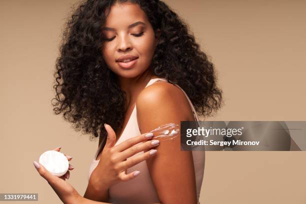 woman applying cream on shoulder while standing against brown background - creme stock-fotos und bilder