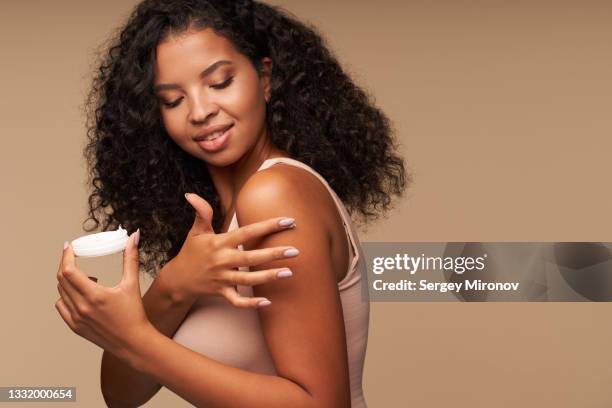 woman applying cream on shoulder against brown background - applying sunscreen stock pictures, royalty-free photos & images