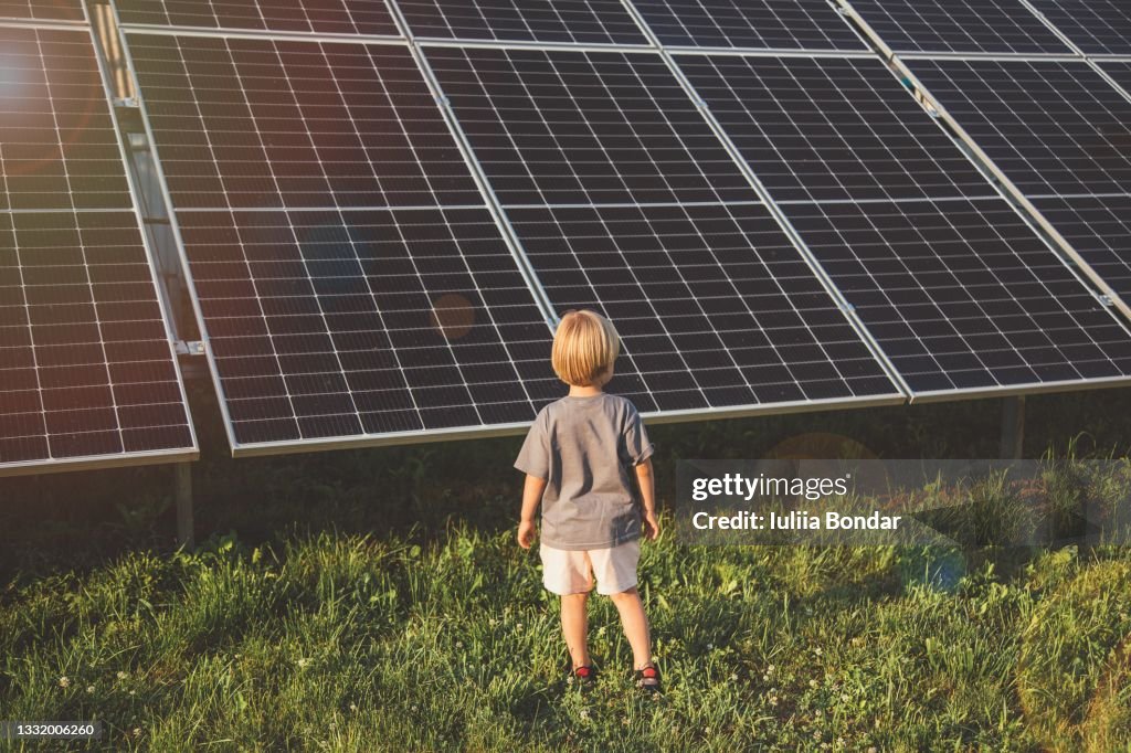 4 year old blonde boy standing in front of small solar panel farm