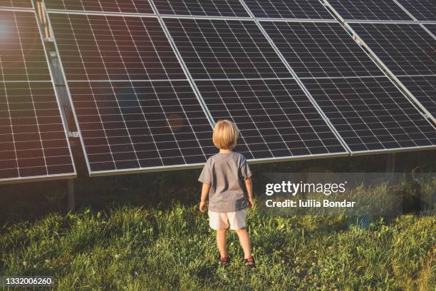 4 year old blonde boy standing in front of small solar panel farm - solar stock-fotos und bilder