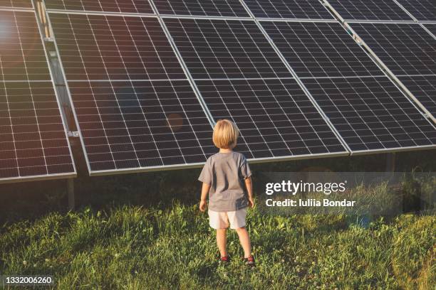 4 year old blonde boy standing in front of small solar panel farm - solar green energy fotografías e imágenes de stock