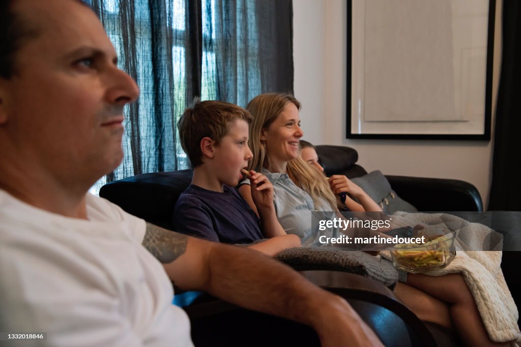 Family of four watching TV in living room.