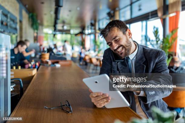 un giovane e felice uomo d'affari sta parlando usando il suo telefono cellulare mentre è seduto nella caffetteria moderna. - man suit using phone tablet foto e immagini stock