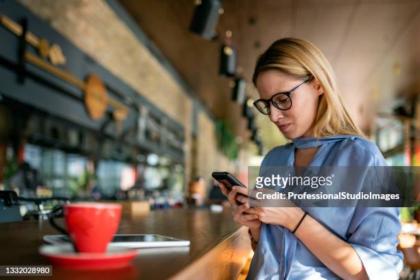a very attractive young businesswoman is enjoying a hot drink in café and making some business plans on her mobile phone. - female worried mobile imagens e fotografias de stock