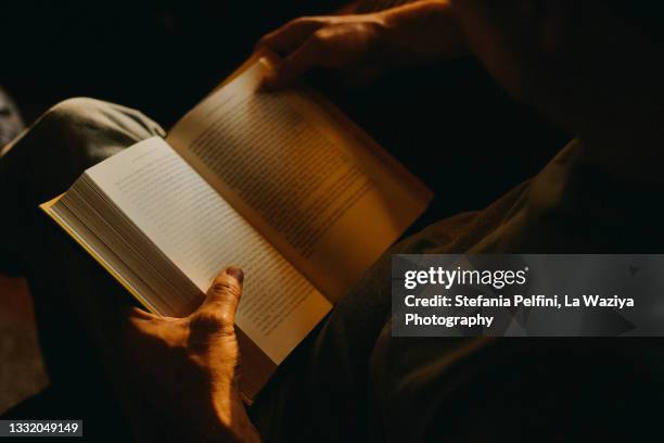 man reading a book indoor at dusk - research literature stock pictures, royalty-free photos & images