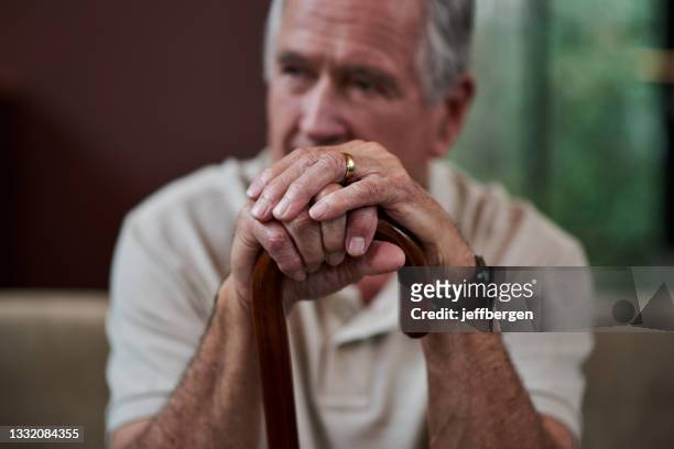 nahaufnahme eines älteren mannes, der zu hause einen gehstock hält - witwer stock-fotos und bilder