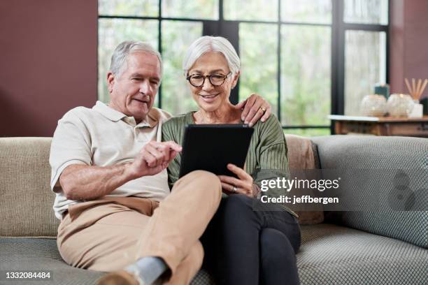 shot of a senior couple using a digital tablet while relaxing on a sofa at home - married imagens e fotografias de stock