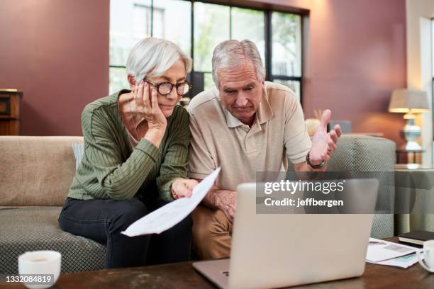 shot of a senior couple using a laptop while going through paperwork at home - erfenis stockfoto's en -beelden