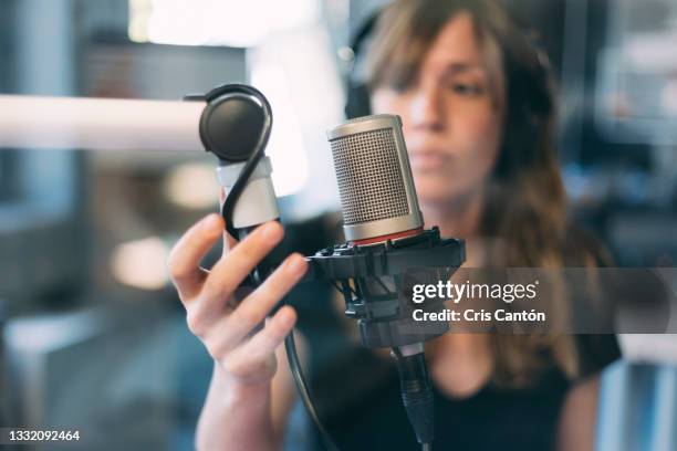 female radio host working in broadcasting studio adjusting microphone - locutor-de-rádio imagens e fotografias de stock