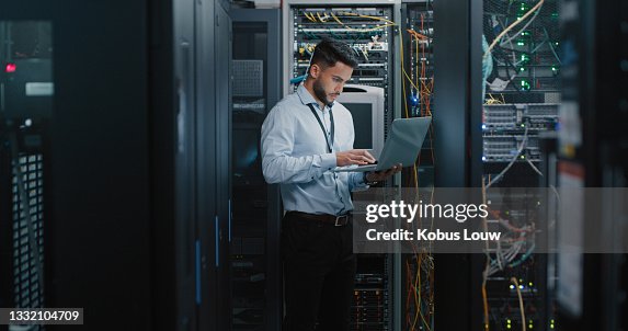 Shot of a young male engineer using his laptop in a server room Shot of a young male engineer using his laptop in a server room
