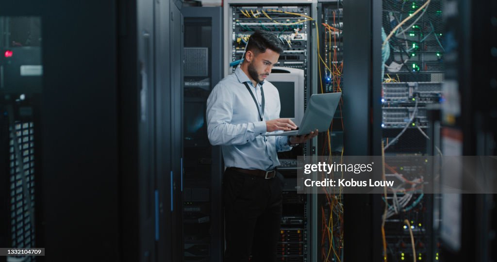 Shot of a young male engineer using his laptop in a server room