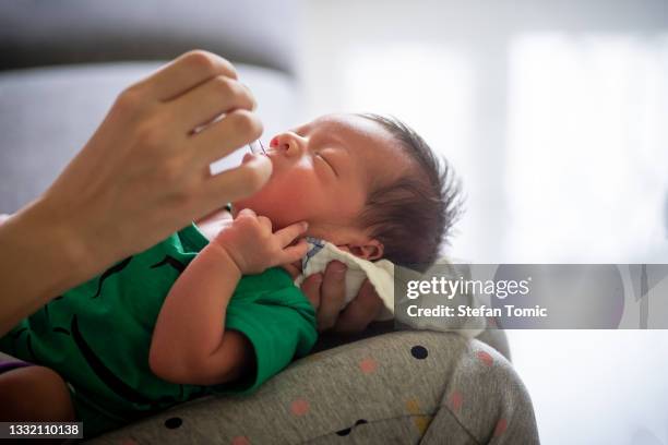 mother giving vitamins and supplements to a newborn baby boy sitting on the sofa in the living room - vitamin drip stock pictures, royalty-free photos & images