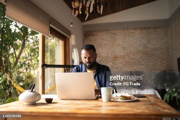 hombre maduro usando computadora portátil trabajando en casa - real businessman isolated no smile fotografías e imágenes de stock