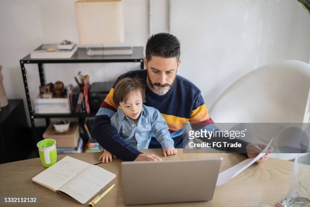 mature man working at home with baby son - boy with special needs - family financial planning stock pictures, royalty-free photos & images