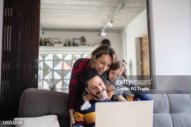 man using laptop and being embraced by wife and special needs son at home - familie laptop stockfoto's en -beelden