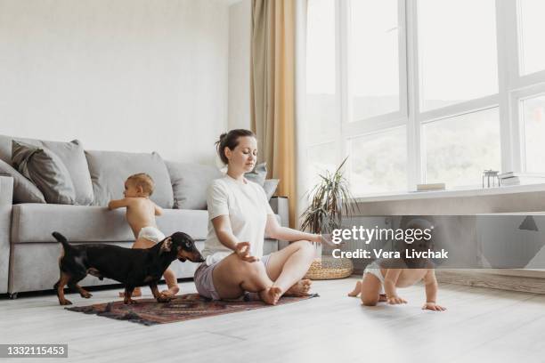 young mom at home doing meditation on the floor with two twin children - three storey stock pictures, royalty-free photos & images