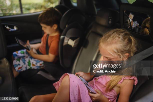 車の後部座席で運転しながら、スマートフォンやデジタルタブレットを使用して兄弟 - child car tablet ストックフォトと画像