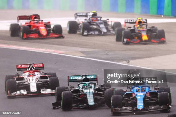 Fernando Alonso of Spain driving the Alpine A521 Renault next to Lance Stroll of Canada driving the Aston Martin AMR21 Mercedes and Kimi Raikkonen of...