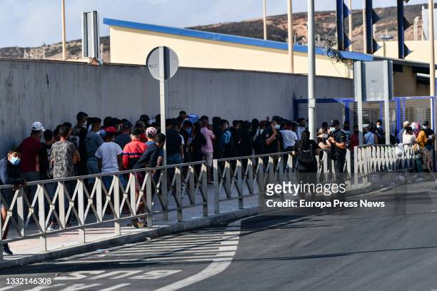 Police officers supervise hundreds of people, mostly Moroccans, queuing at the asylum office located at the Tarajal border separating Ceuta from...