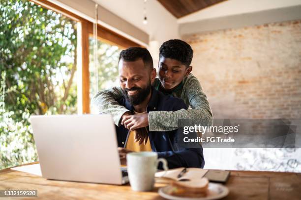 sohn umarmt vater, während er zu hause arbeitet - asian smiling father son stock-fotos und bilder