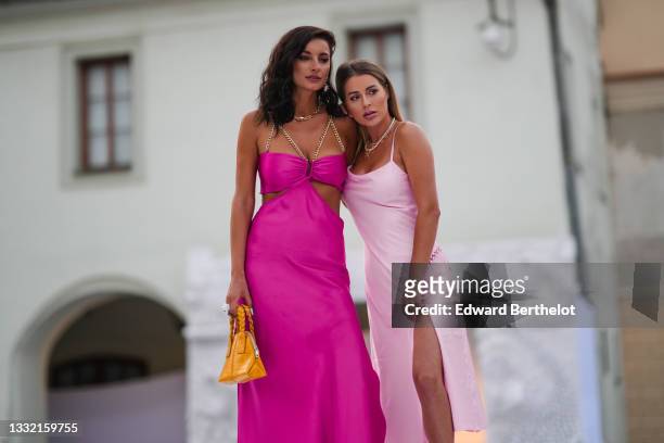 Ioana Visanescu wears a pink / fuchsia shiny satin cut-out / V-neck / split flowing dress with gold chain tank-top shoulders, gold large pearl...