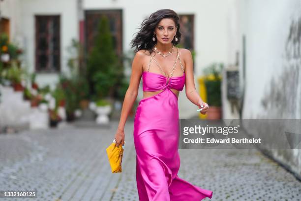 Ioana Visanescu wears a pink / fuchsia shiny satin cut-out / V-neck / split flowing dress with gold chain tank-top shoulders, gold large pearl...