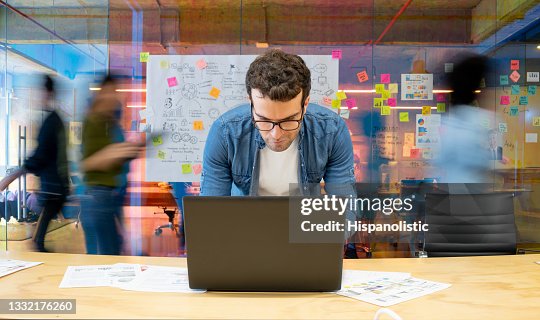 Man working at a creative office using his computer and people moving at the background Man working at a creative office using his computer and people moving at the background