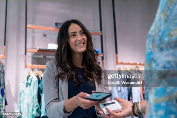 smiling woman doing contactless payment at clothes store - shop pay stockfoto's en -beelden