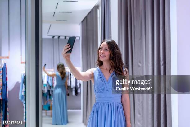 woman taking selfie while wearing blue dress near changing room in boutique - blue dress imagens e fotografias de stock