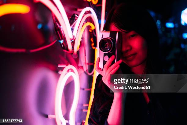 young female photographer photographing neon lighting with retro style camera - fluorescente - fotografias e filmes do acervo