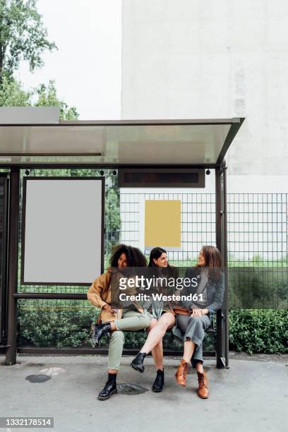 women talking while sitting at bus stop - bushaltestelle stock-fotos und bilder