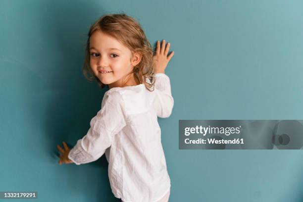 smiling girl leaning on blue wall - kid leaning stock pictures, royalty-free photos & images