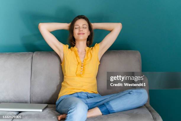 woman with hands behind head sitting by laptop on sofa at home - hands behind head stock pictures, royalty-free photos & images