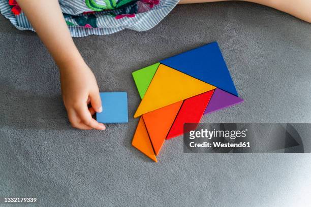 woman playing with multi colored tangram on sofa - tangram foto e immagini stock