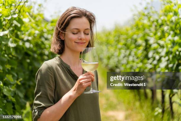 smiling woman smelling wine while standing at vineyard - gusto foto e immagini stock