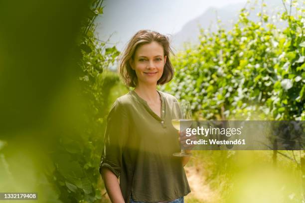 smiling woman holding wineglass while standing at wine field - brown hair drink wine stock pictures, royalty-free photos & images