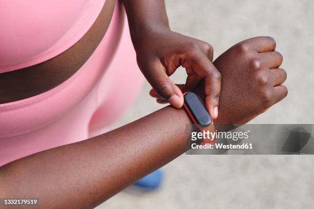 woman checking time on smart watch while standing on footpath - reloj inteligente fotografías e imágenes de stock