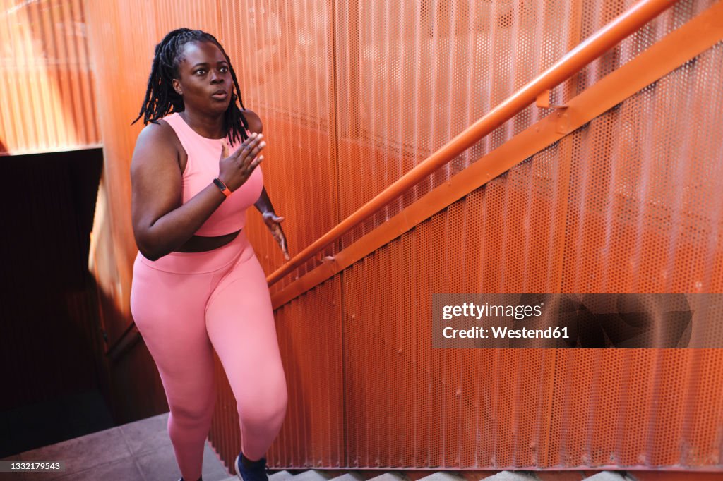 Plus size woman in sports clothing running on staircase