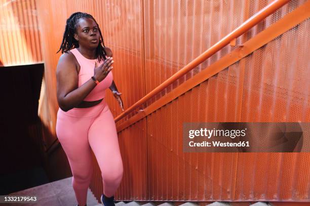 plus size woman in sports clothing running on staircase - curvy black women stockfoto's en -beelden